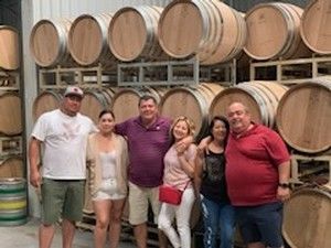 Group of people posing by wine barrels in a winery; indoors.