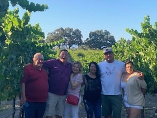 Group of six people smiling in a vineyard, sunny day.