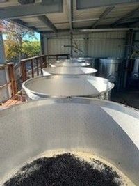 Large stainless steel vats lined up inside a metal building, filled with dark contents.