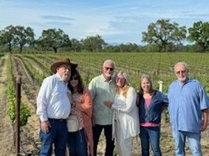 Group of people at a vineyard, posing for a photo. Trees and grapevines in background.