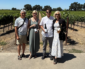 Four people holding wine bottles in a vineyard; sunny day.