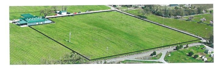 Aerial view of a rectangular green field outlined in black with buildings on the left and a road along the bottom.