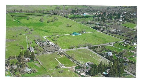 Aerial view of green fields and buildings, likely farmland or a ranch.