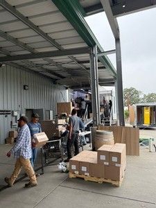 People loading boxes onto a truck under a covered loading dock. Outdoors, industrial setting.