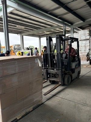 Forklift moving a large stack of wrapped cardboard boxes in a warehouse.