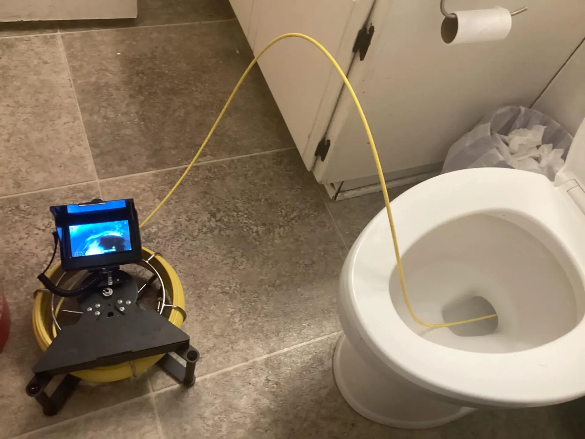 Small robot with a yellow hose in a bathroom beside a white toilet.