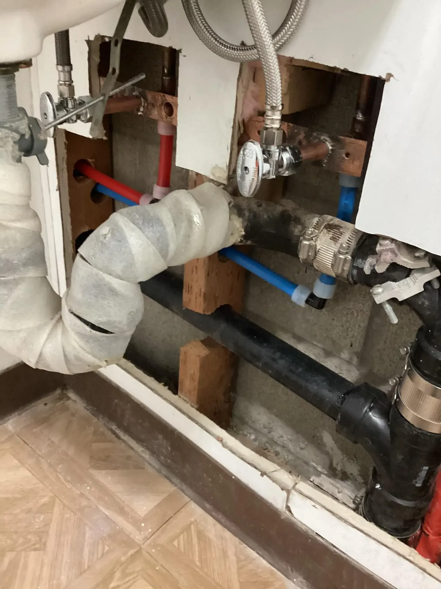 Under-sink plumbing with exposed pipes, valves, and a wrapped drain hose during repair