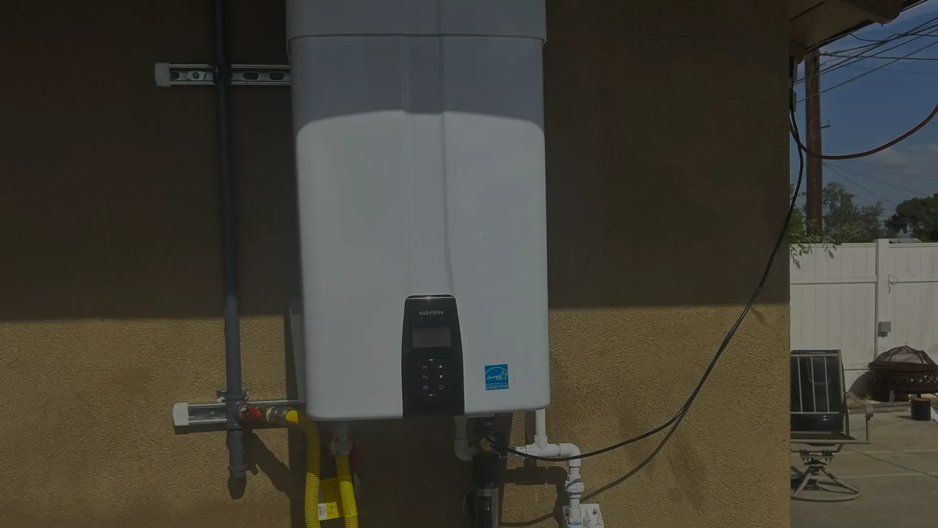 White wall-mounted appliance on an exterior stucco wall, with cables and a small black control panel.
