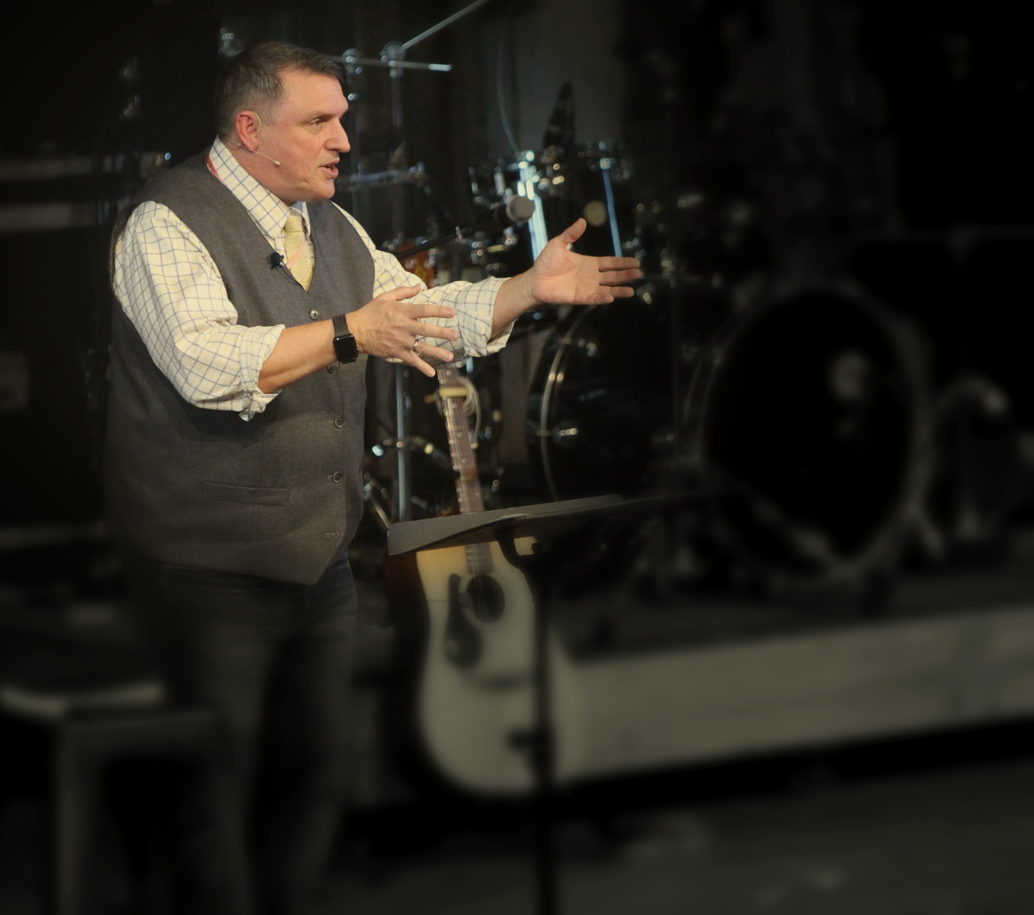 Pastor Dr Bill Giovannetti preaching from a music stand in front of drums