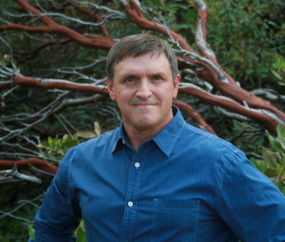 A man in a blue shirt is standing in front of a tree