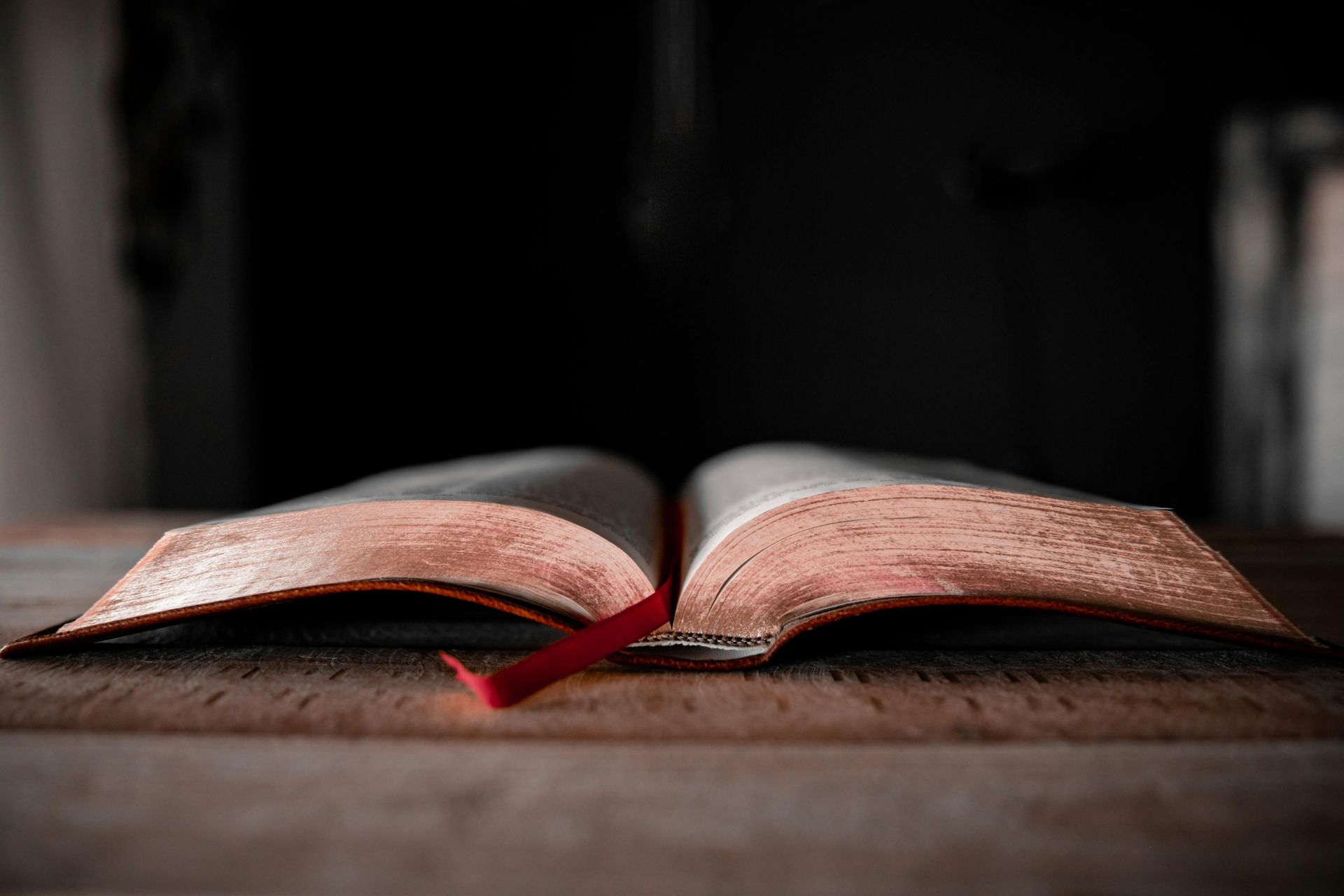 Open book on a wooden surface with a red ribbon bookmark.