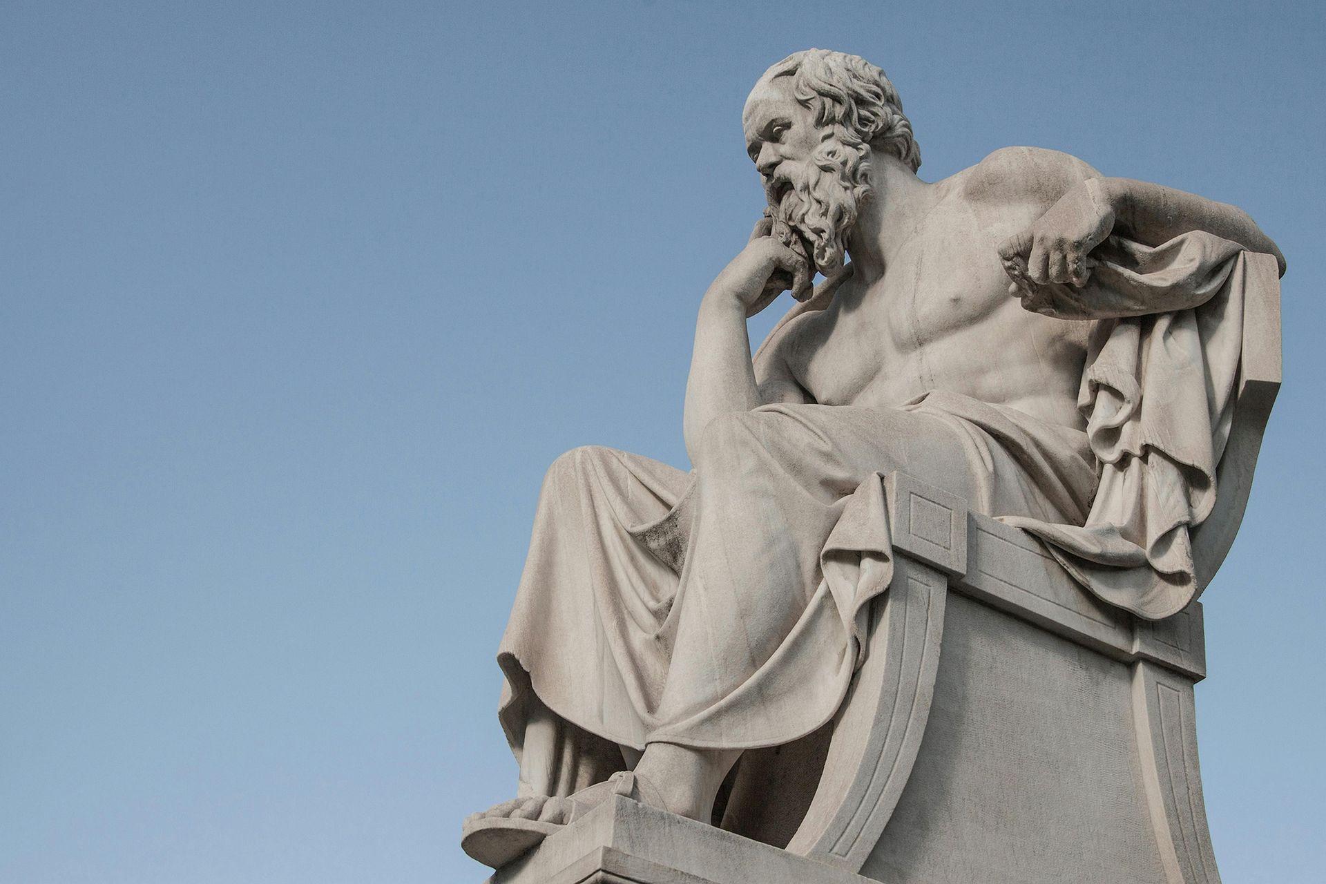 A statue of a man with a beard is sitting on a rock.