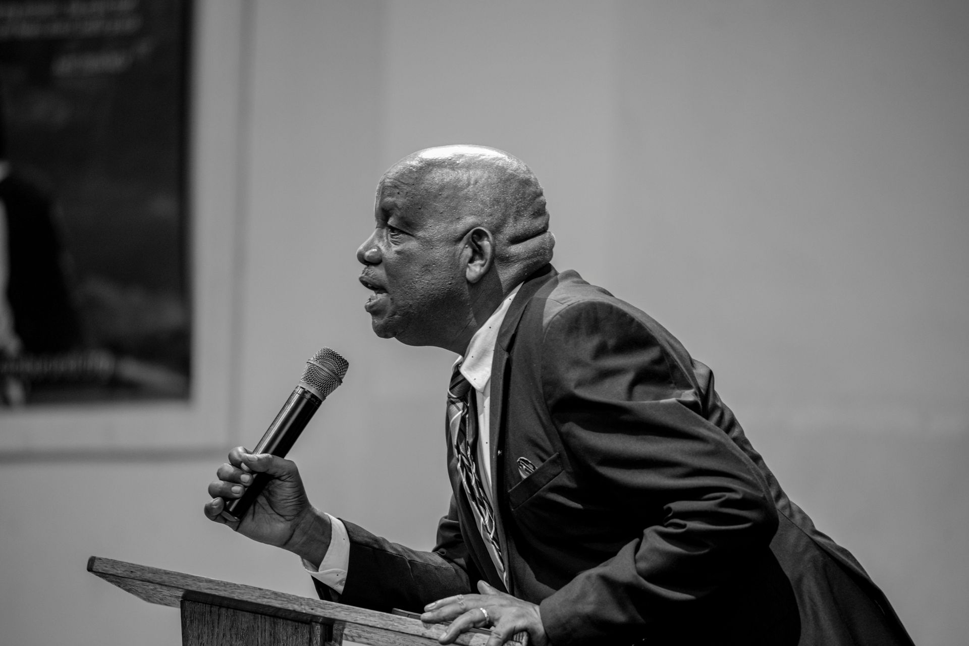 A man in a suit is standing at a podium holding a microphone.