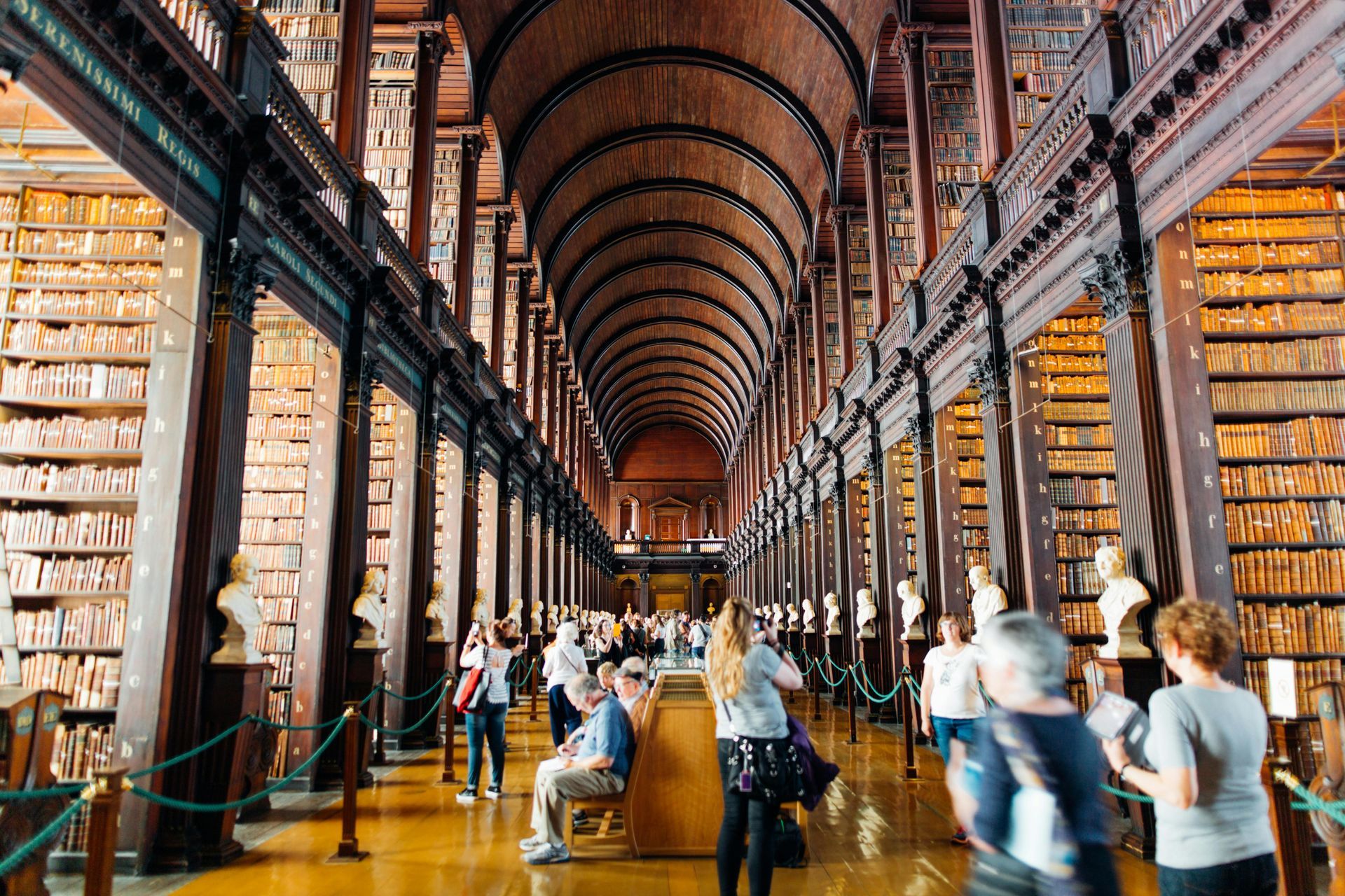 A group of people are walking through a library filled with lots of books.