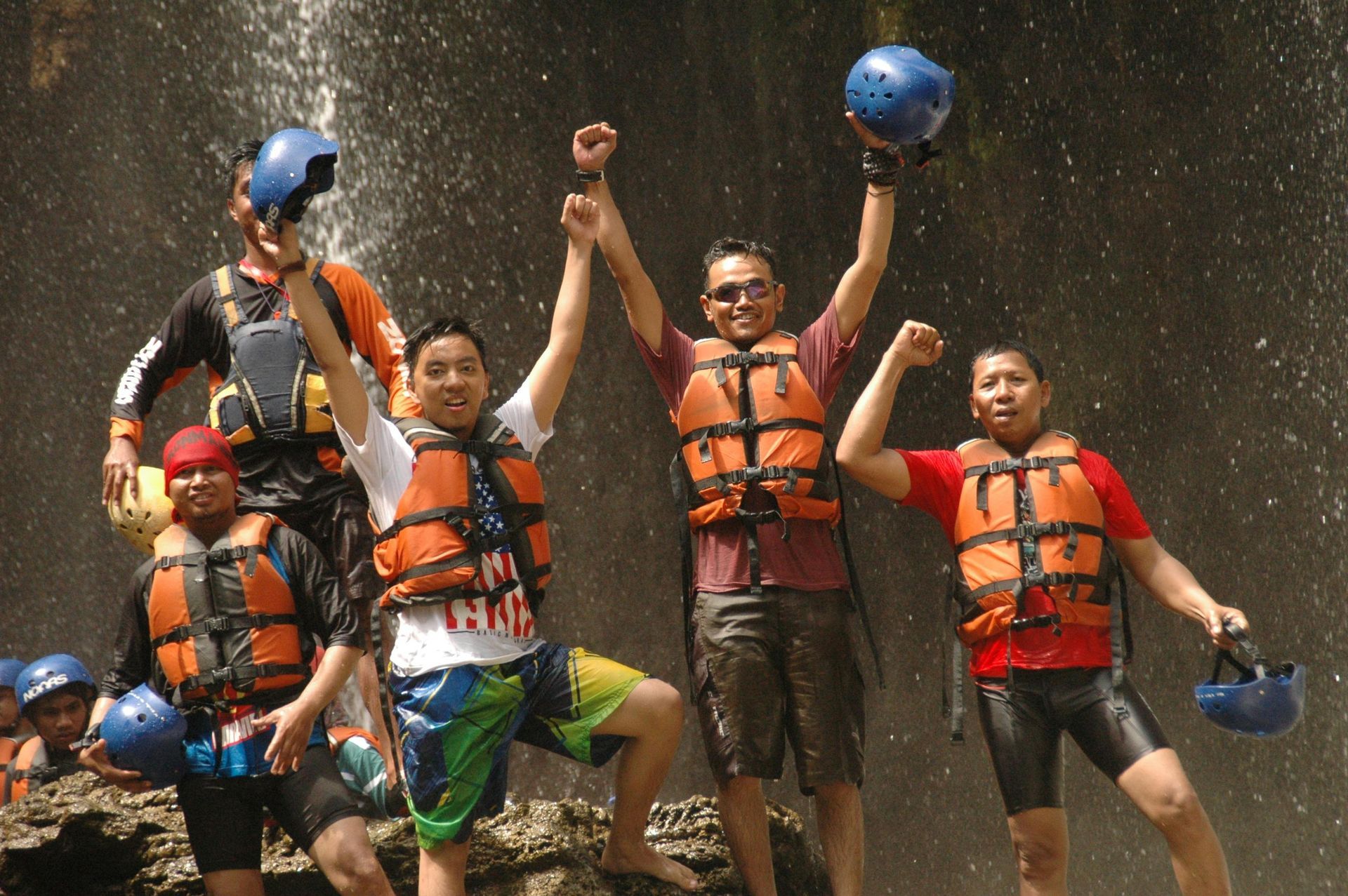 A group of people standing in front of a waterfall with their arms in the air