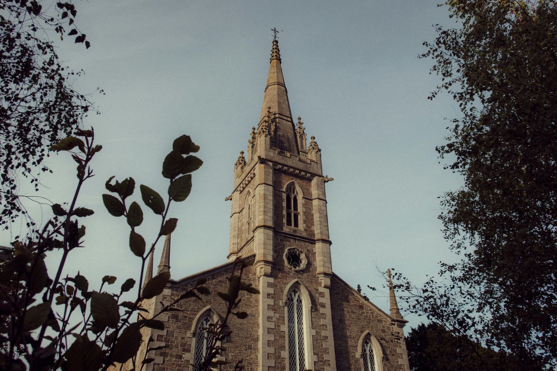 Stone church with tall spire framed by tree branches.
