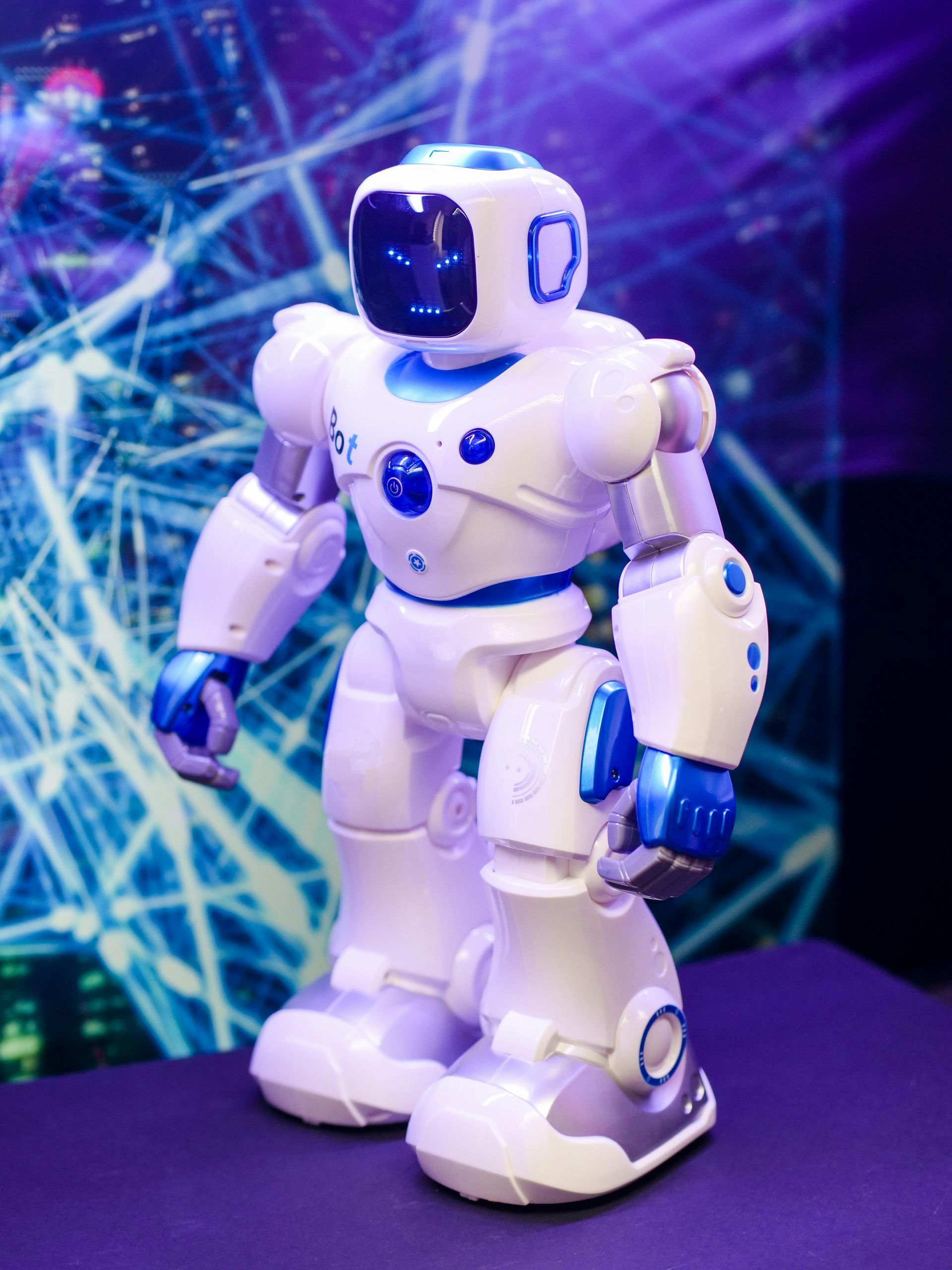 White and blue humanoid robot, standing on a dark surface in front of a blue digital background.