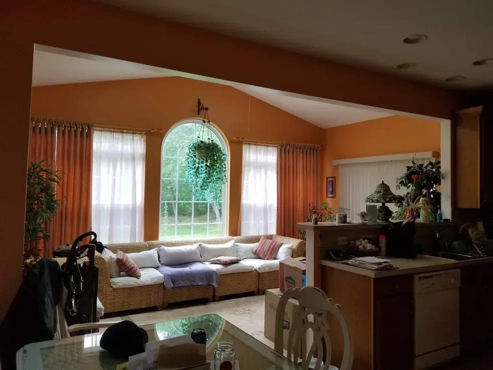 Living room with arched window, orange walls, sectional sofa, and kitchen view.