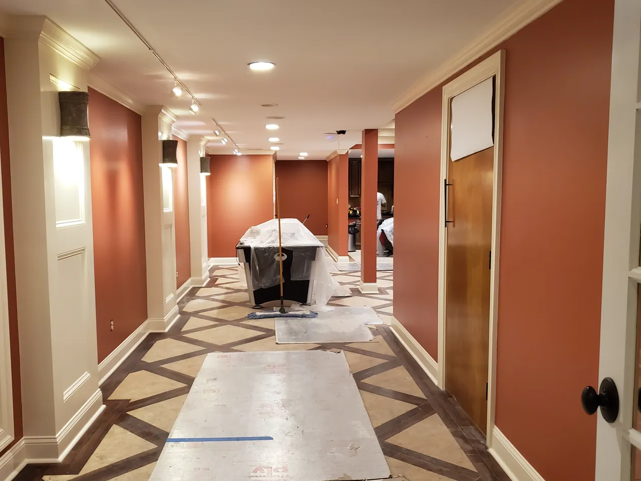 Long hallway with brick-colored walls, patterned carpet, and several doors; some furniture covered with plastic.