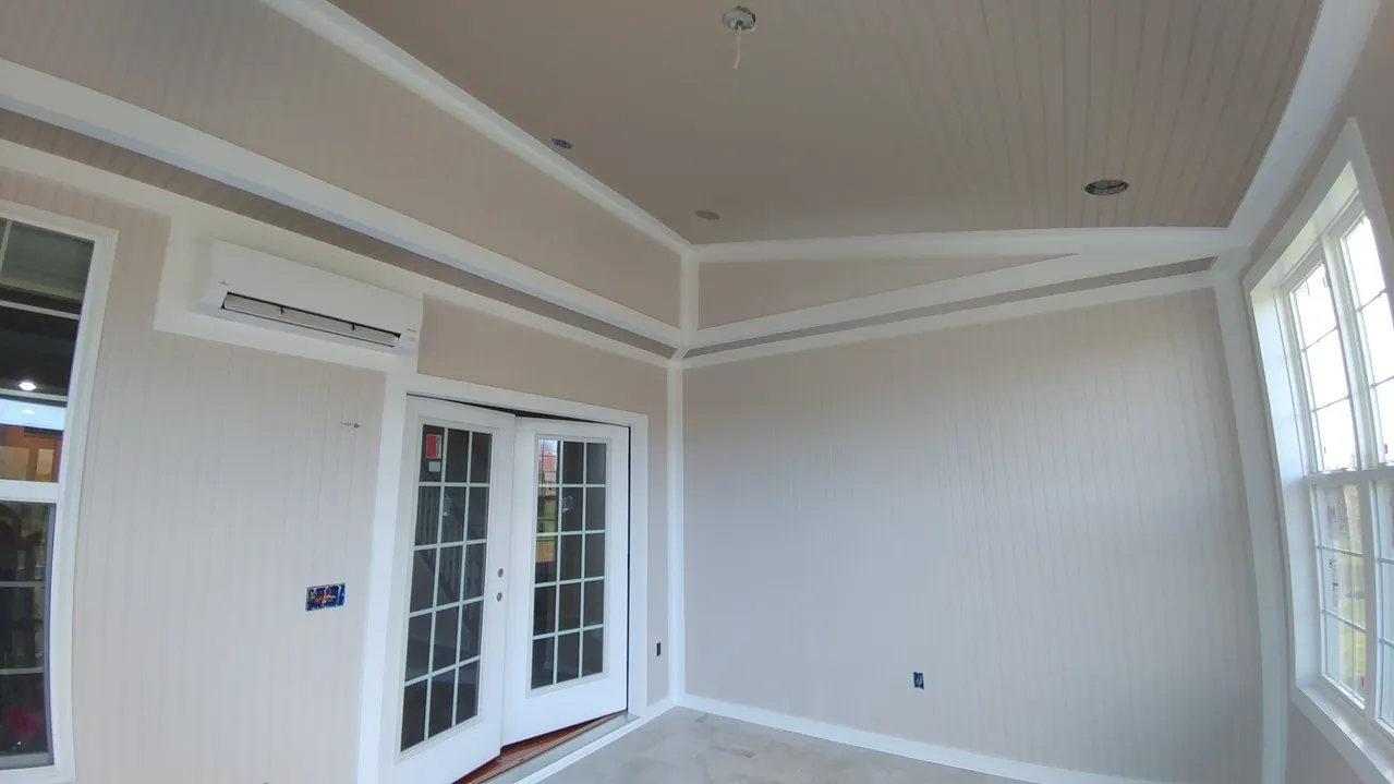 Interior of a room with light beige walls, white trim, and a beige ceiling. French doors and windows are present.