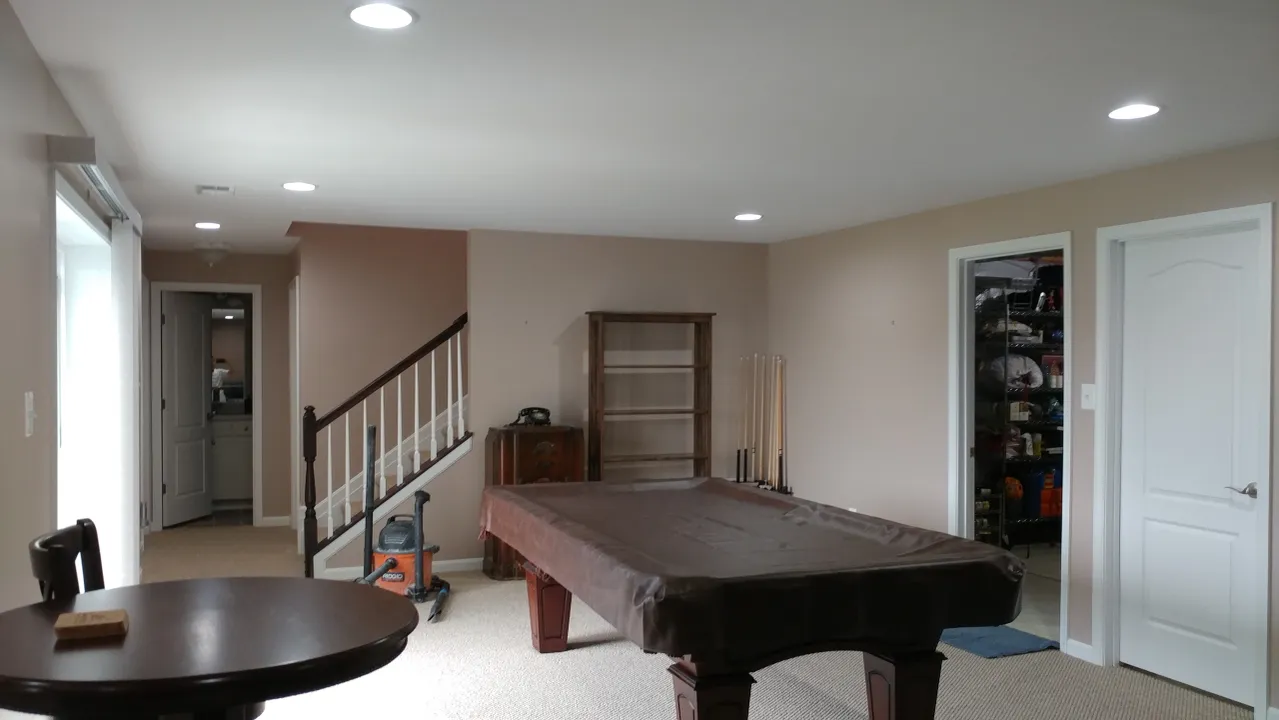 A room with a pool table, stairs, and a round table. White and tan walls.