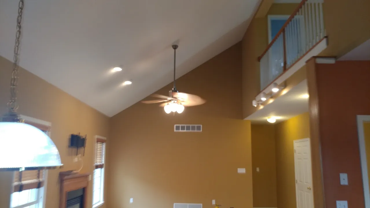 Interior view of a living room with a high ceiling, a ceiling fan, and a loft area with a railing.
