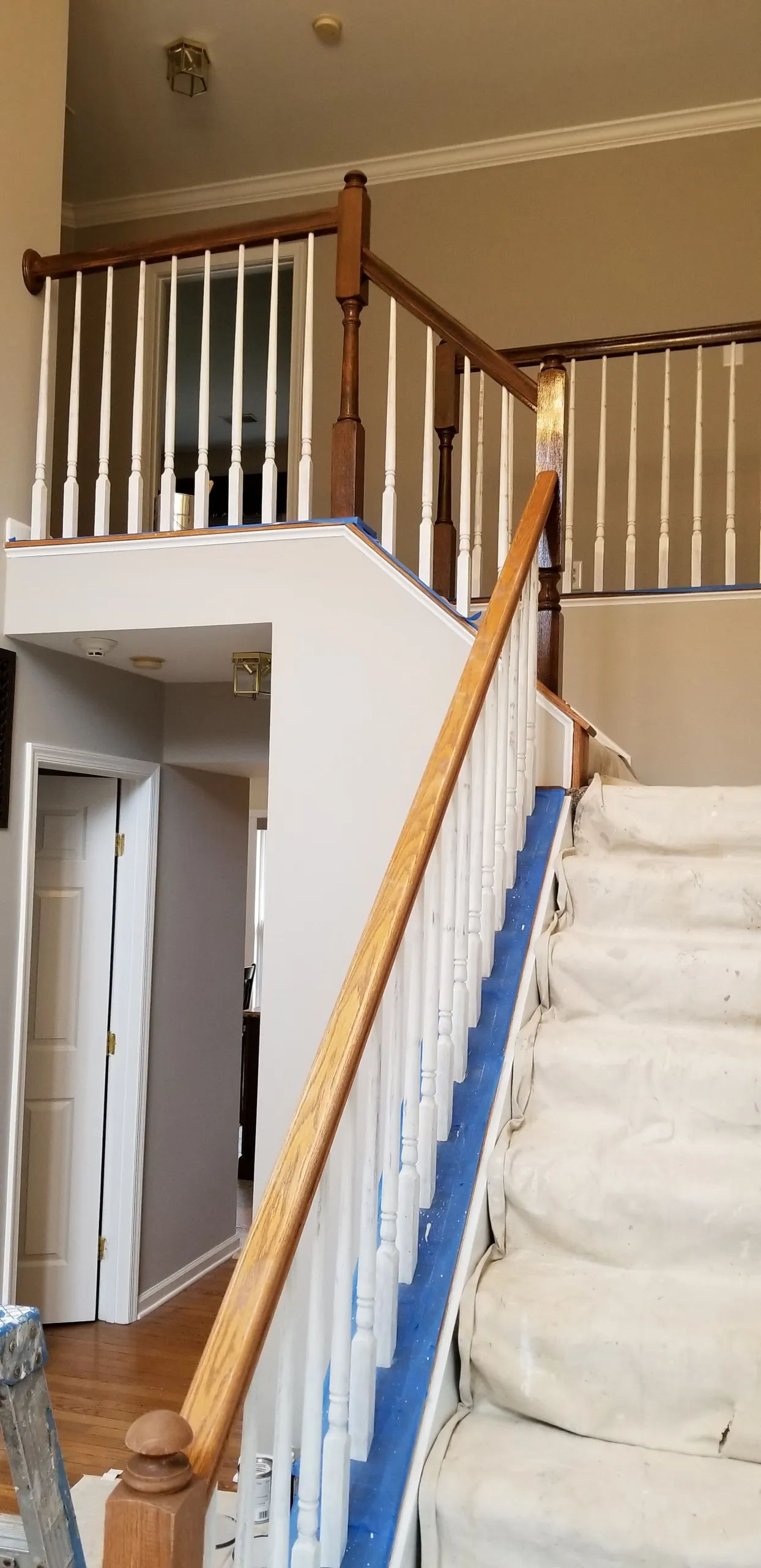 A staircase with white spindles, wooden handrails, and beige carpet. Blue tape lines the carpet edges.
