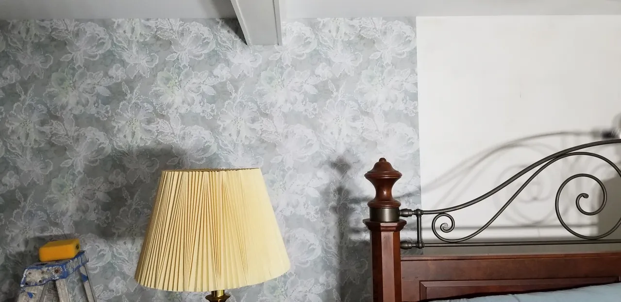 Bedroom scene with a bed, wallpaper, and a lamp. The lamp has a textured lampshade.