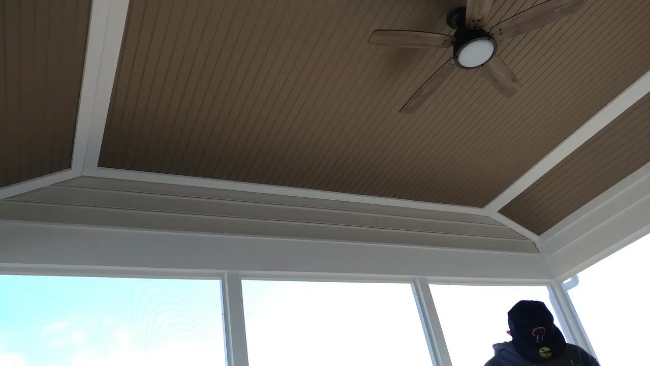 Brown ceiling with white trim, a ceiling fan, and large windows with a person visible.