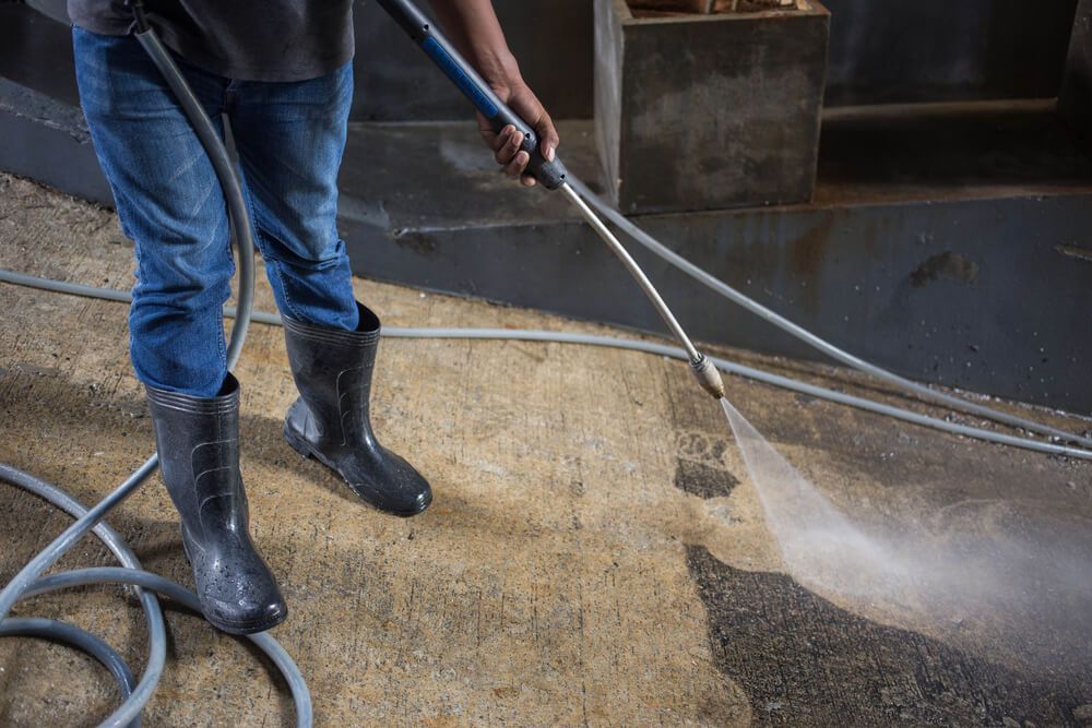 Person in boots using a pressure washer on a concrete surface.