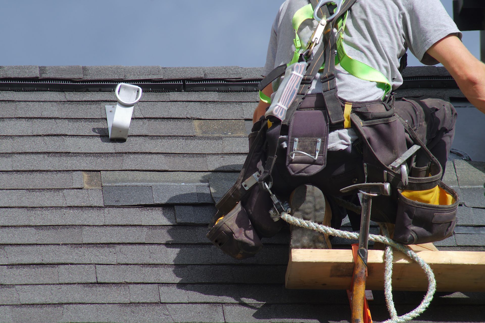 Roofer in safety harness working on asphalt shingle roof.