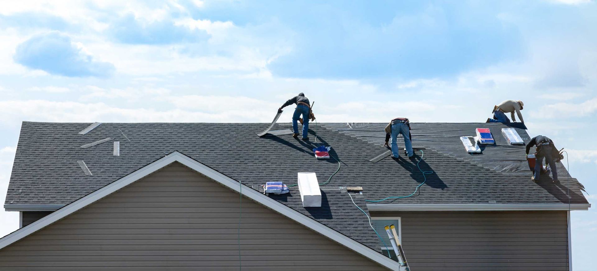 Roofing contractors are fixing the roof against the blue sky, installing shingles on a house.