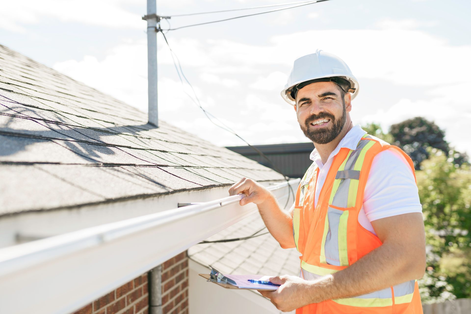 Roof Inspection - Roofer worker in a hard hat, holding a clipboard, standing on the steps of an old