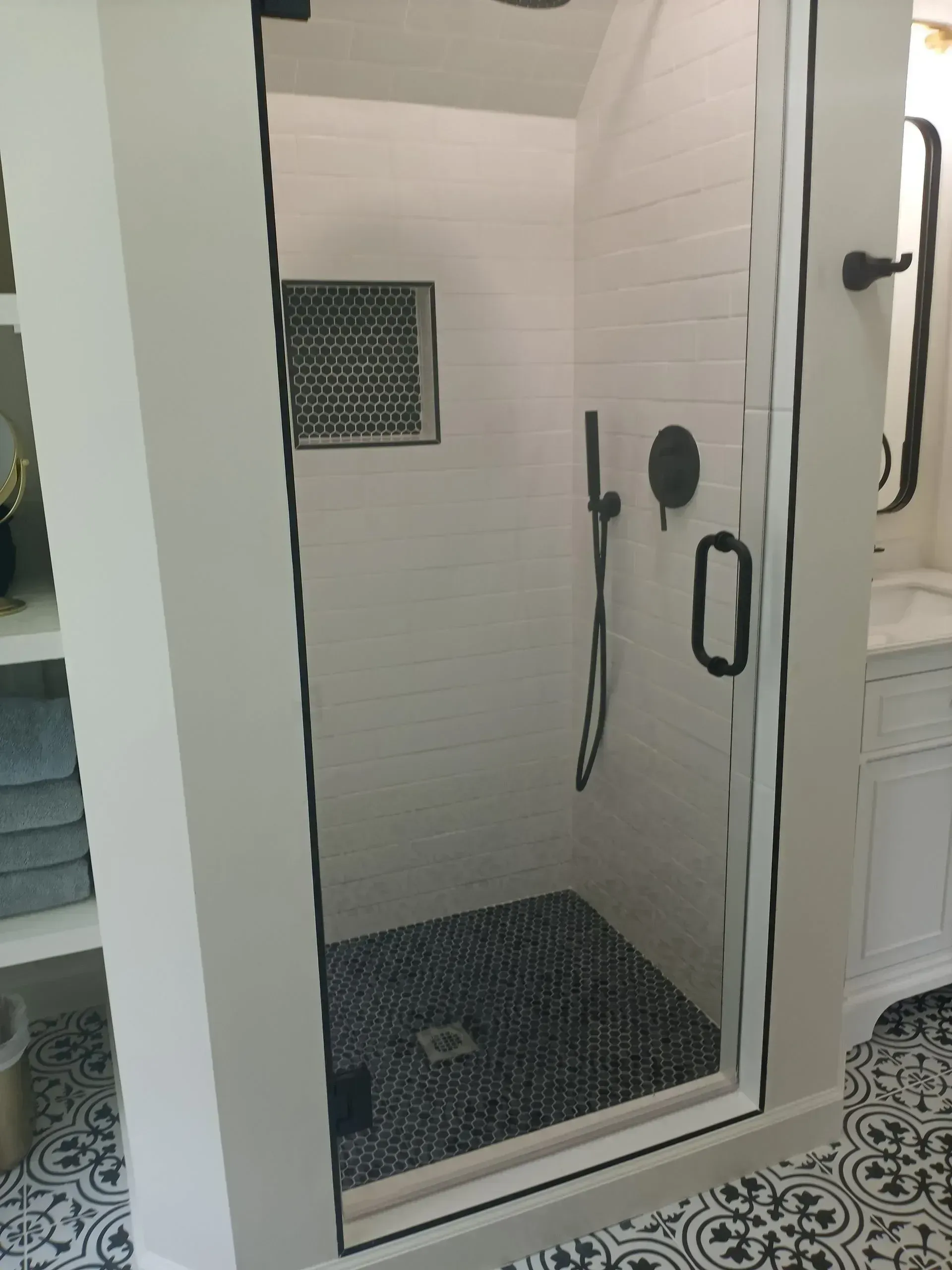 Glass shower stall with tiled floor, white walls, and black shower fixtures