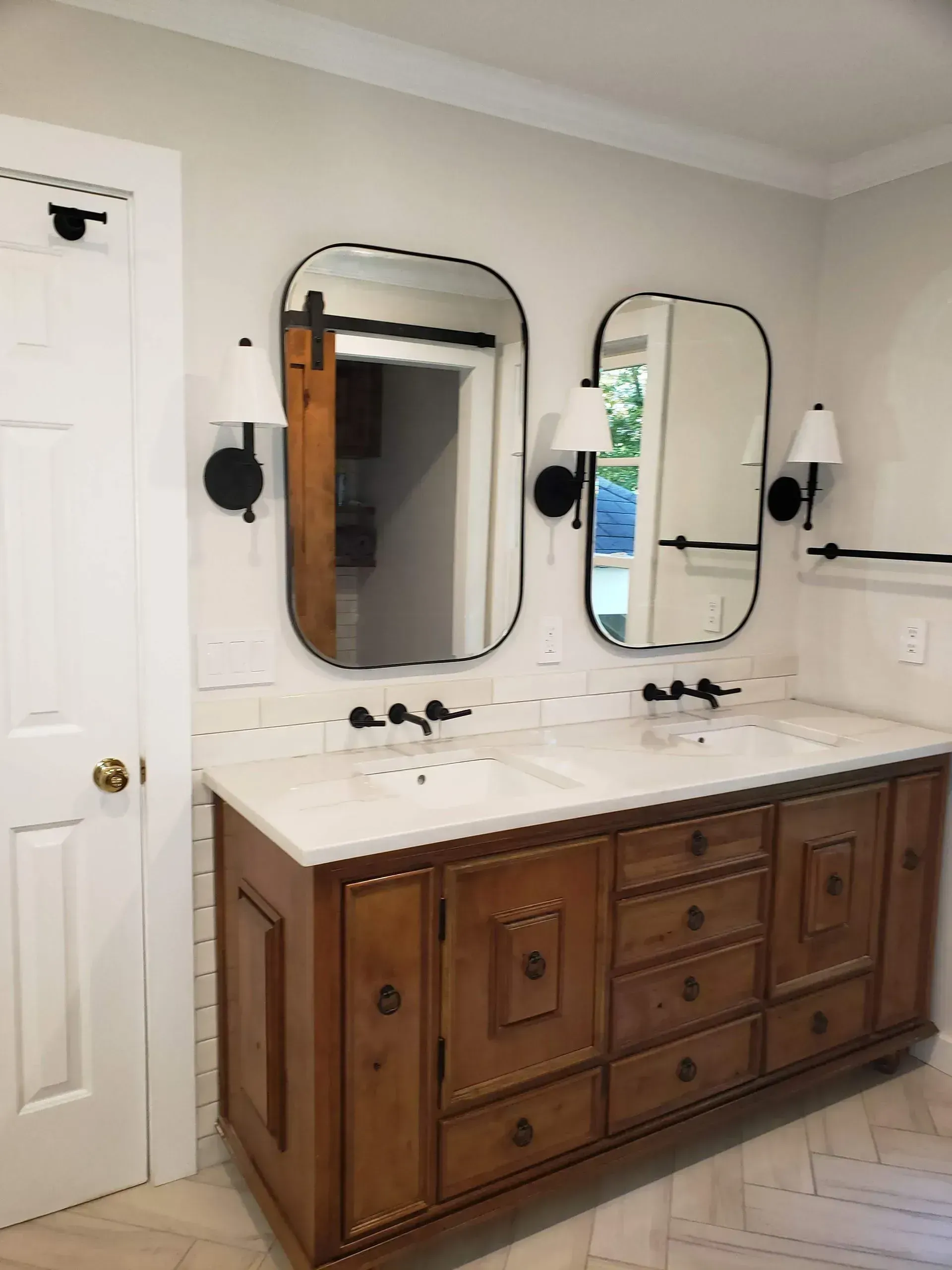 Bathroom vanity with double mirrors, white countertop, and wooden cabinets under wall sconces