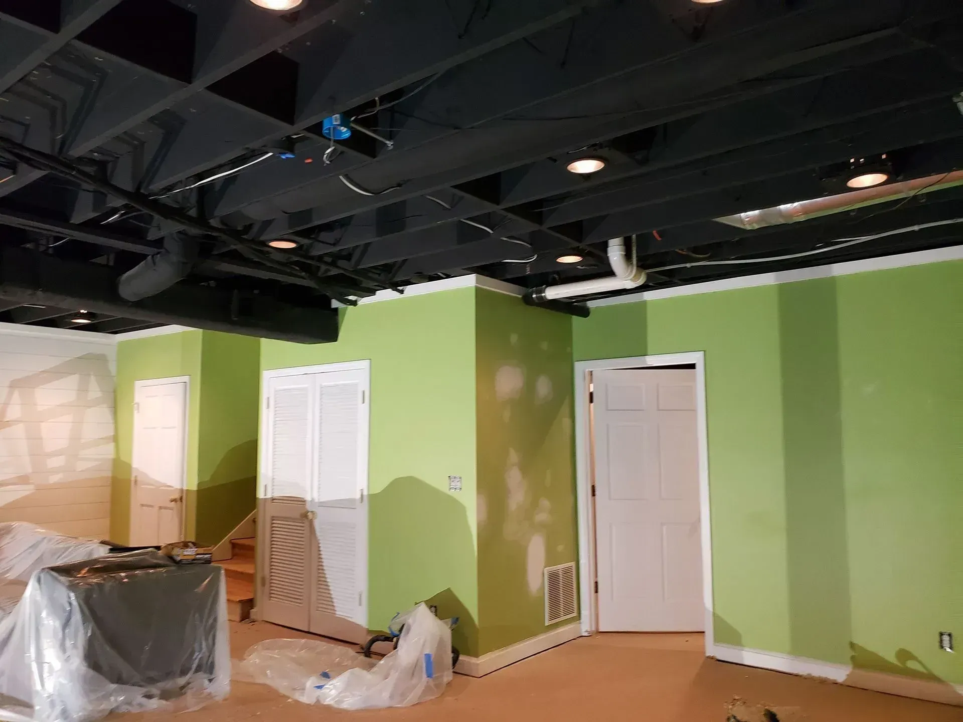 Empty room under renovation with green walls, white doors, and exposed ceiling ducts