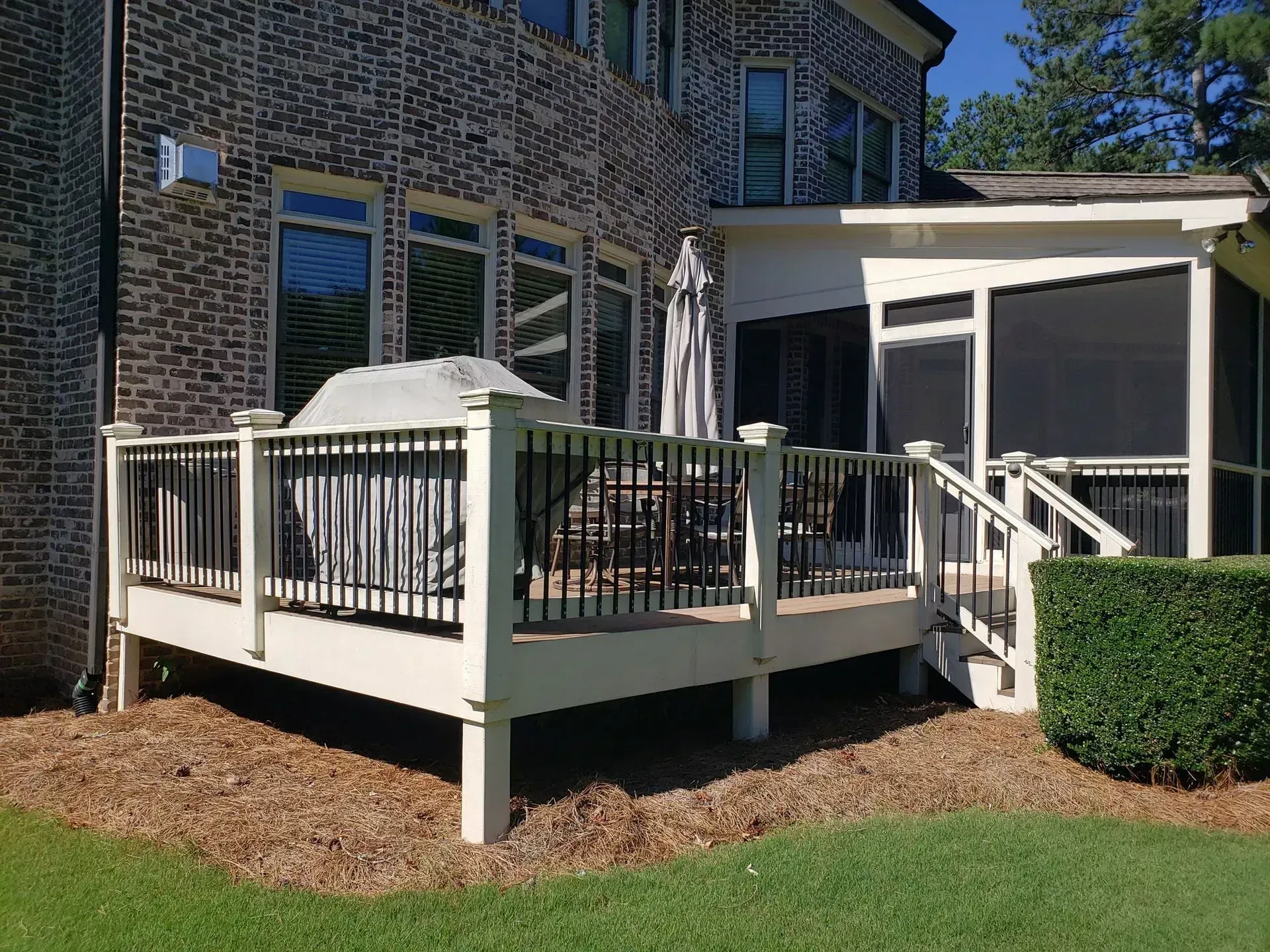 Brick house deck with white railings, patio umbrella, and sliding glass doors in a landscaped yard
