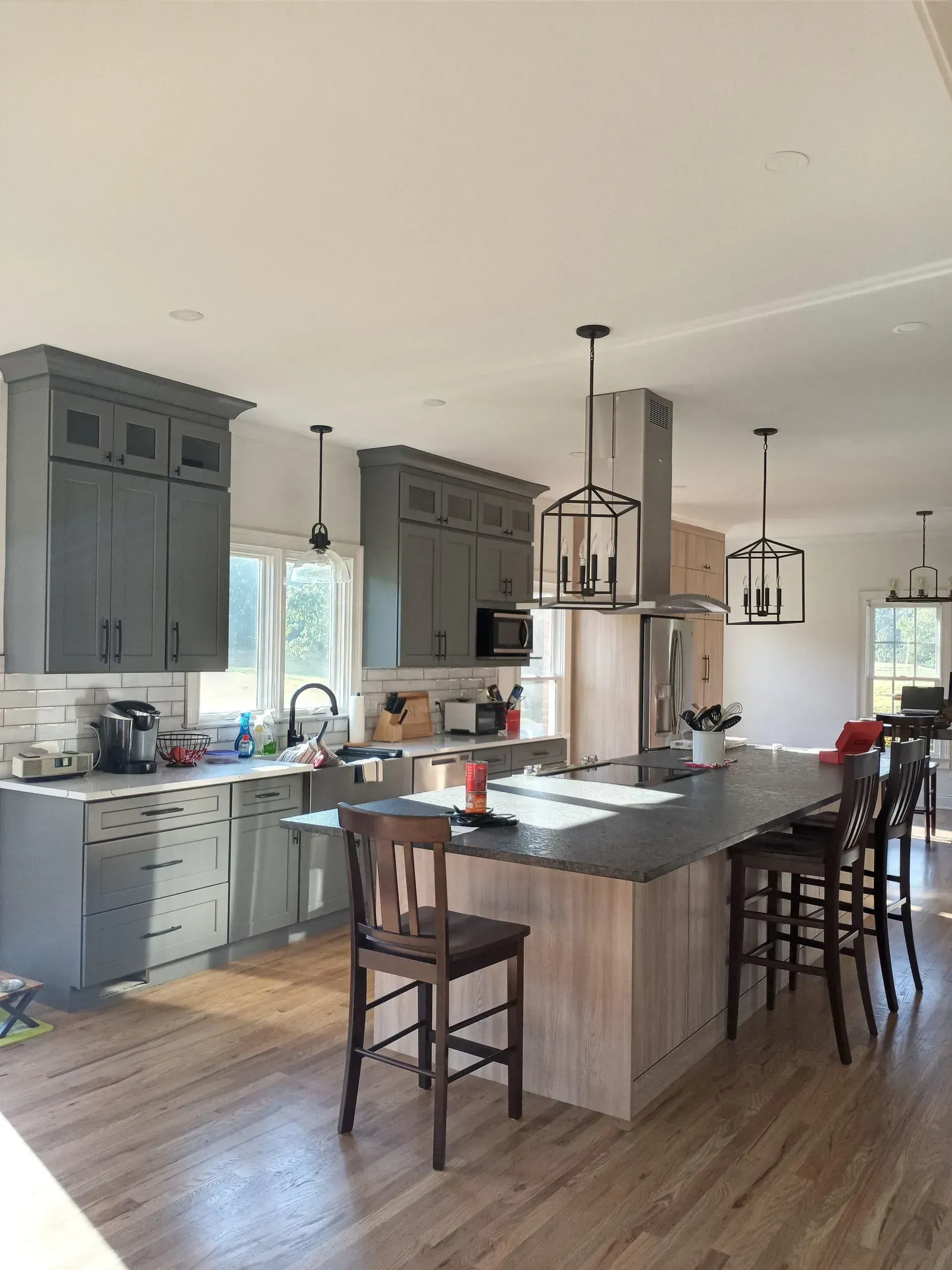Bright kitchen with gray cabinets, wood floors, and a large island with barstools and pendant lights.