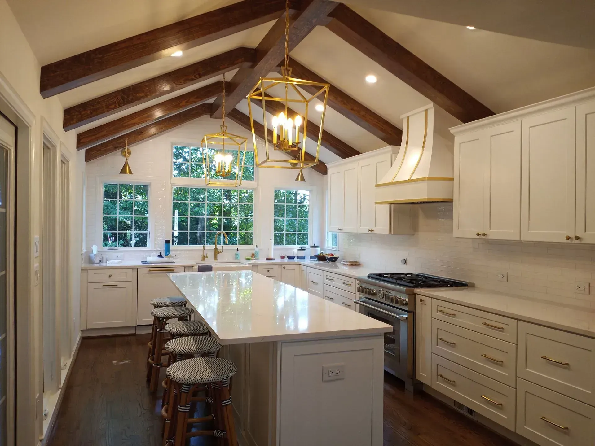 Bright modern kitchen with white cabinets, wooden beams, marble island, and large windows.