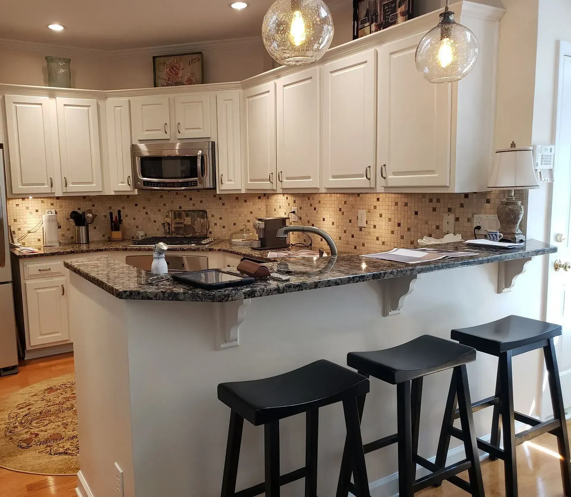 Modern kitchen with white cabinets, granite island, and three black stools under pendant lights