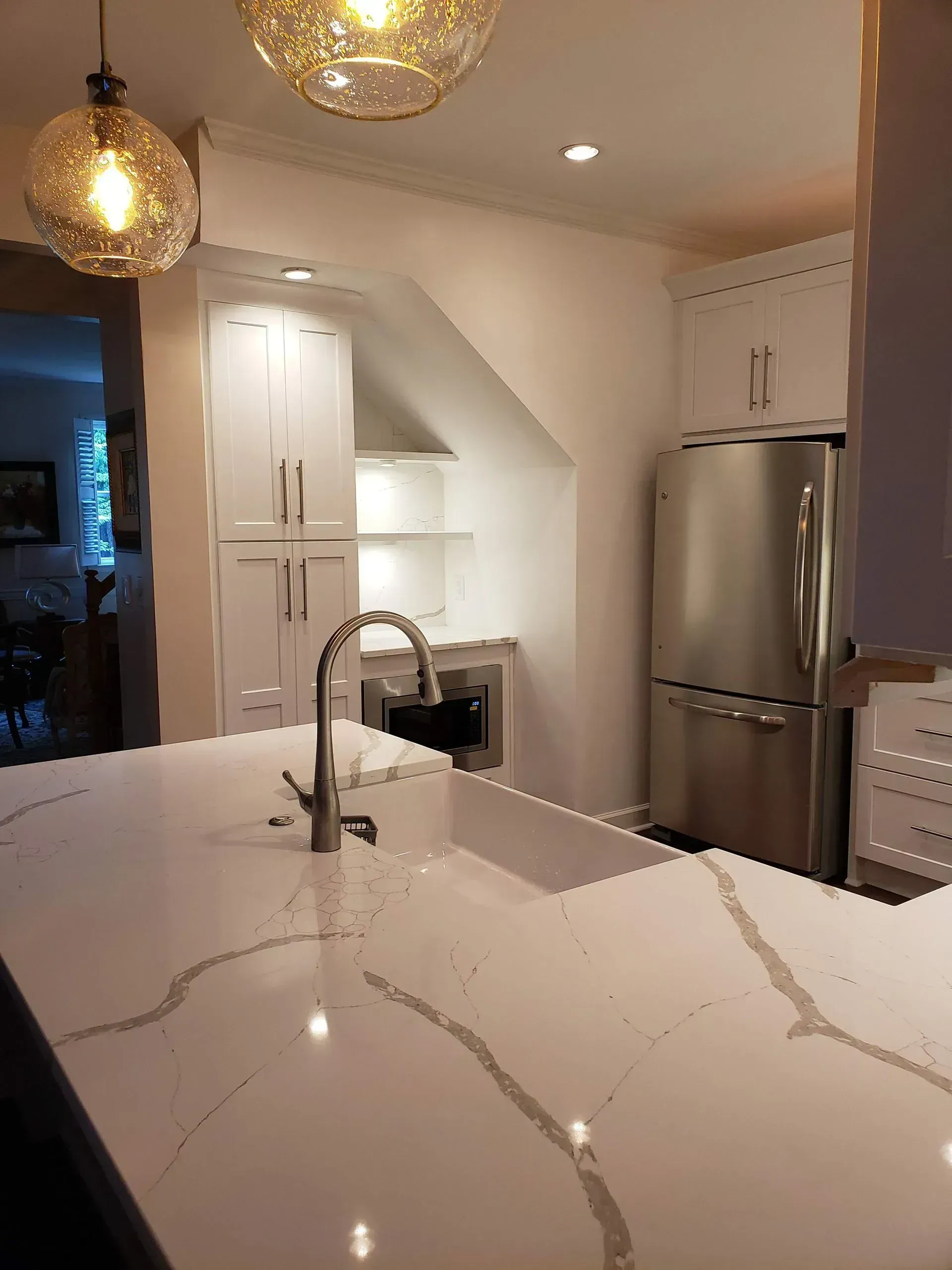 Modern white kitchen with marble island, stainless steel fridge, and pendant lights