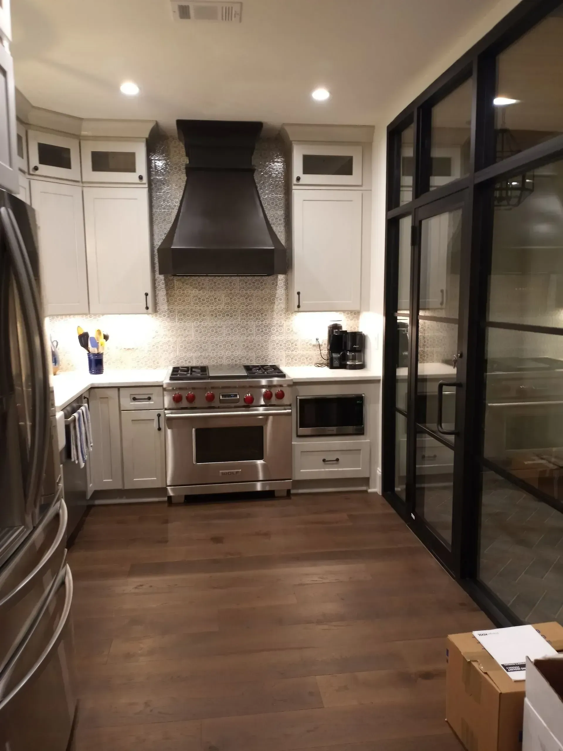 Narrow modern kitchen with stainless steel stove, white cabinets, dark wood floor, and glass wall panels.