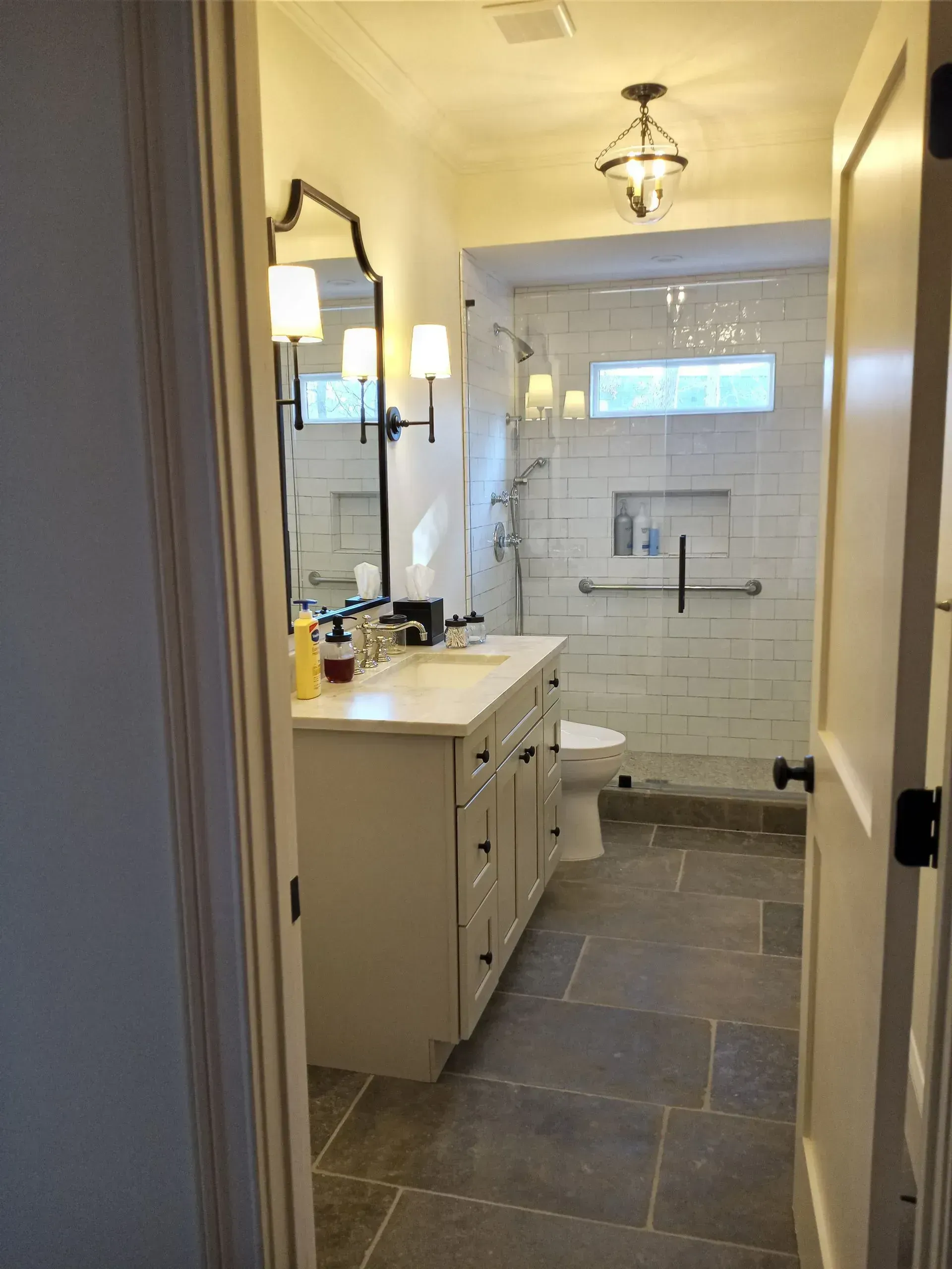 Narrow bathroom hallway leading to a white vanity and a tiled shower with a window.