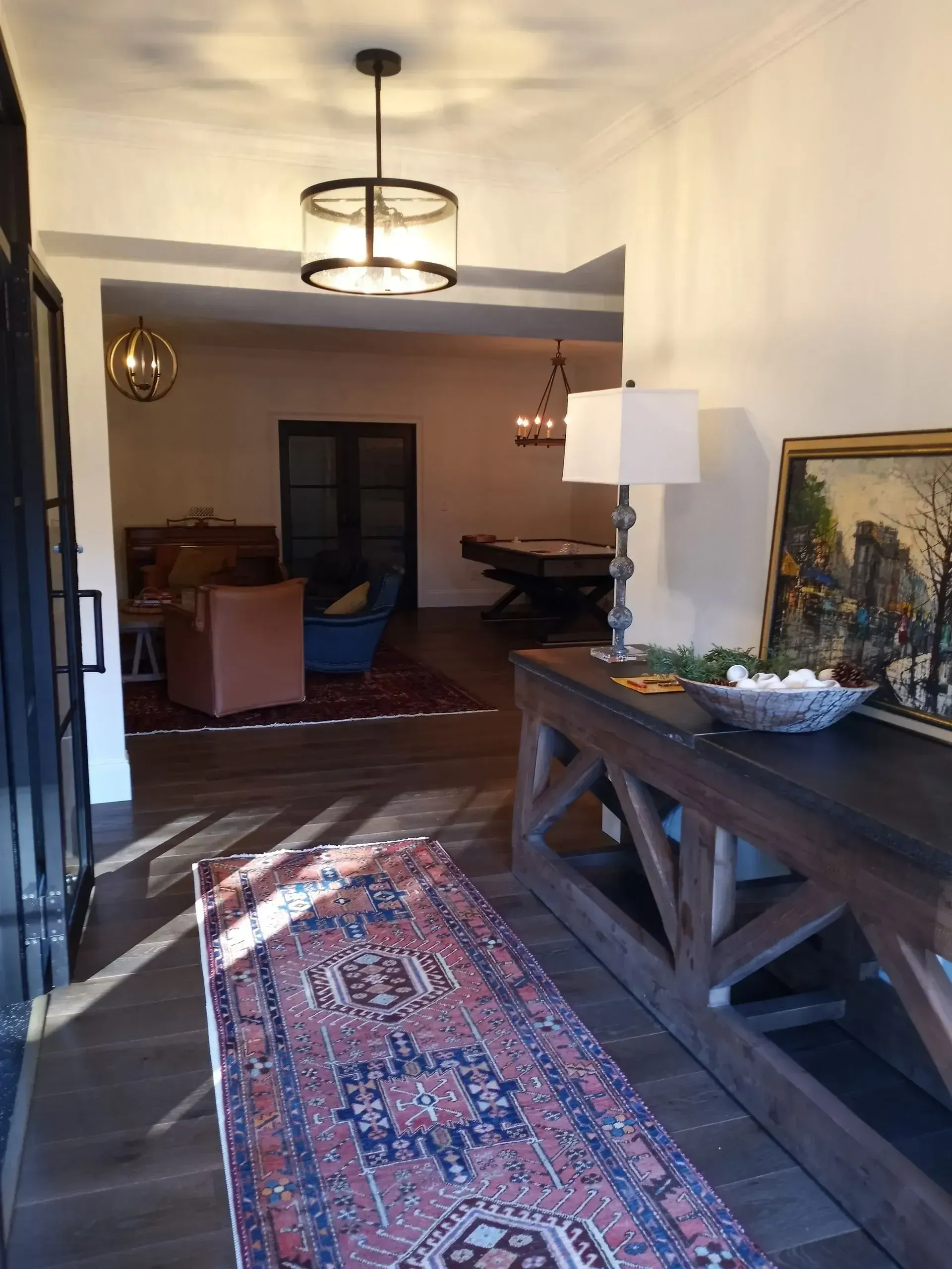 Dim living room with wooden table, patterned rug, pendant lights, and a chair in the background.