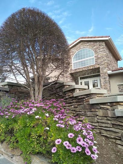 A house with a stone wall and flowers in front of it.