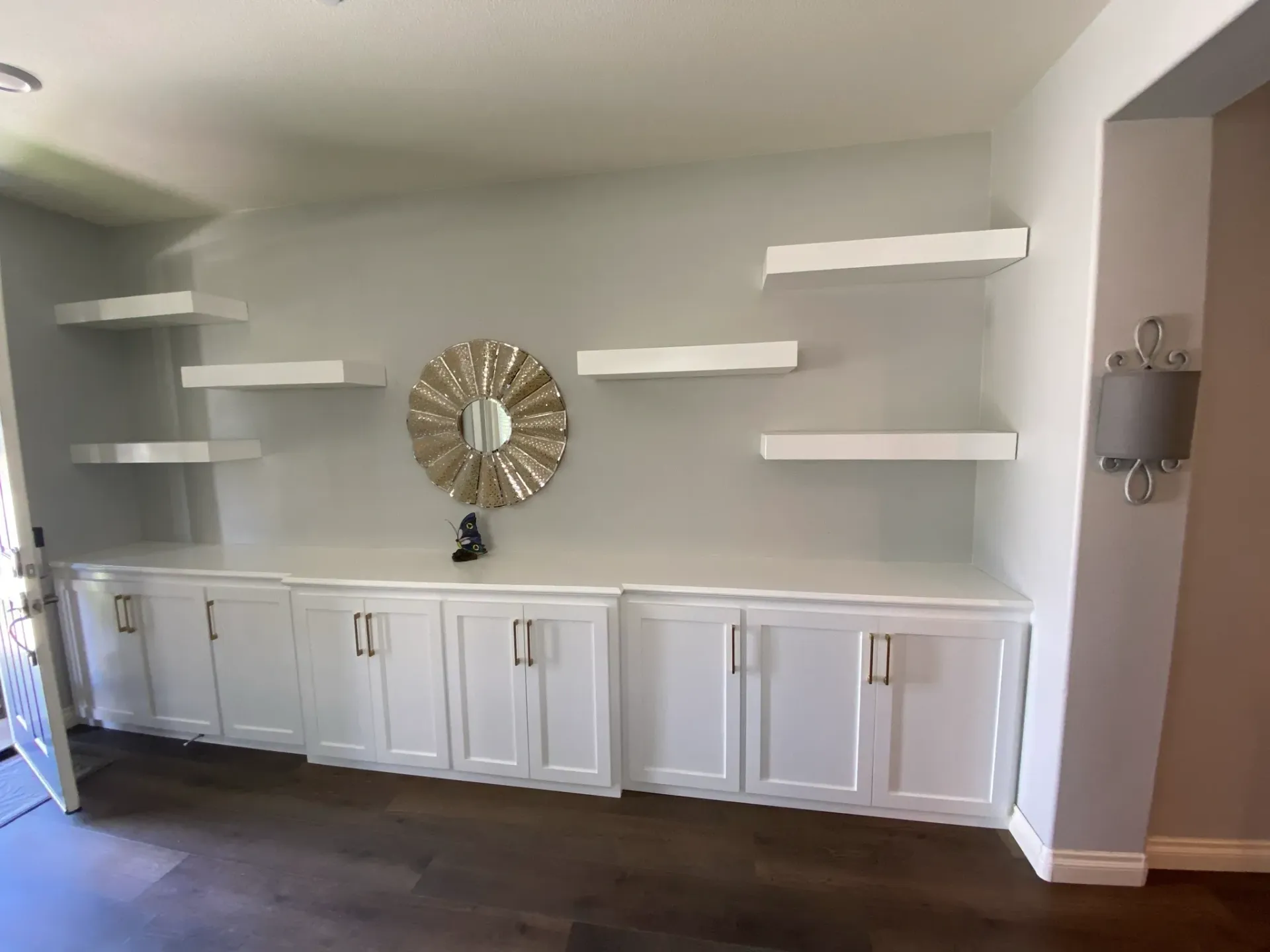 A living room with white cabinets and shelves and a mirror on the wall.