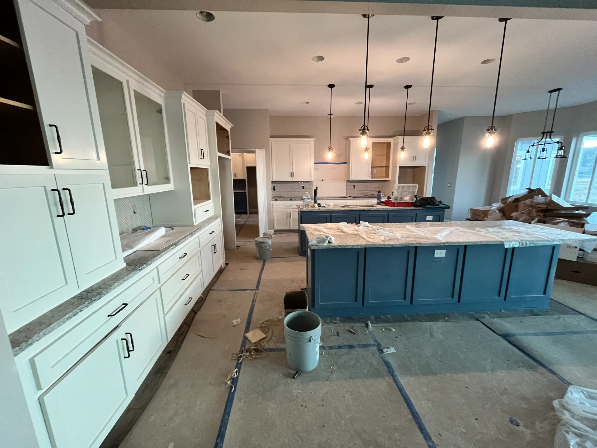 A kitchen under construction with white cabinets and a blue island.