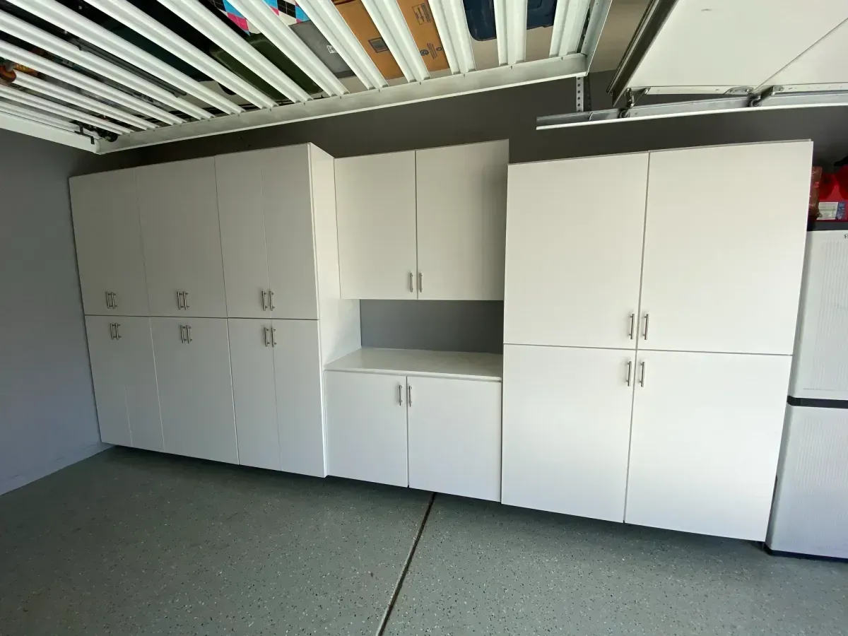 A garage with a lot of white cabinets and a refrigerator