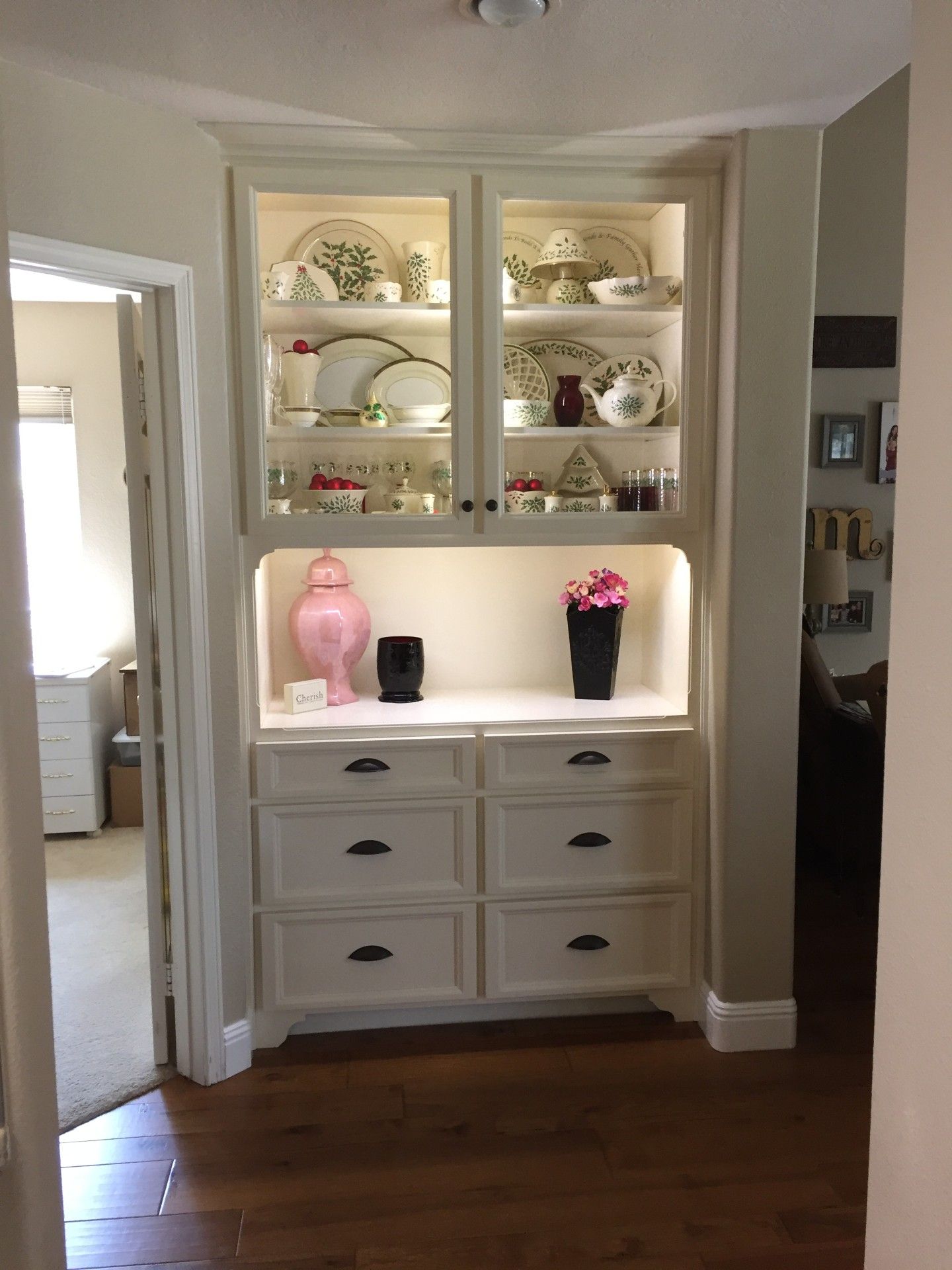 A white cabinet with drawers and shelves filled with plates and vases