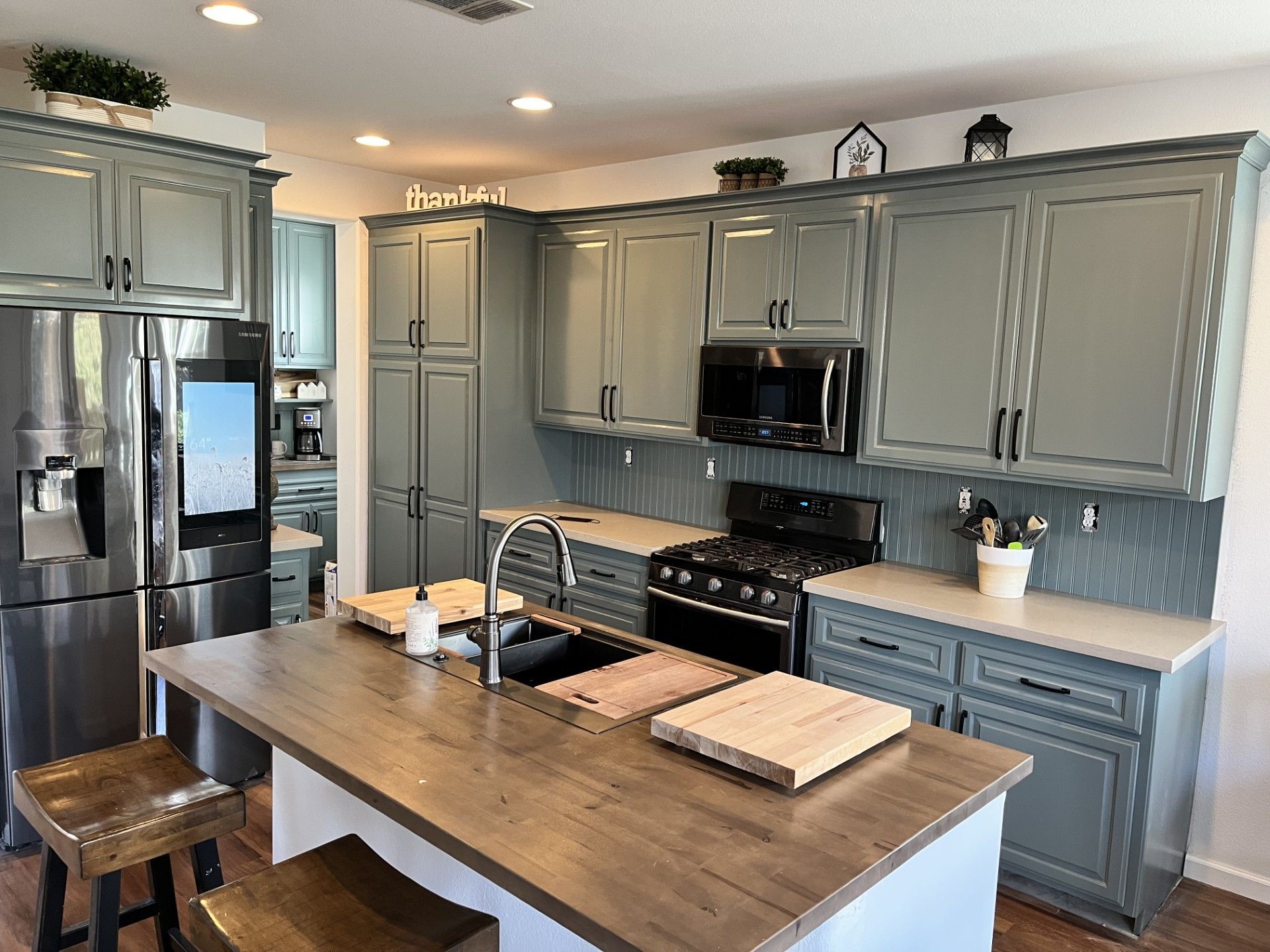 A kitchen with gray cabinets , stainless steel appliances and a large island.